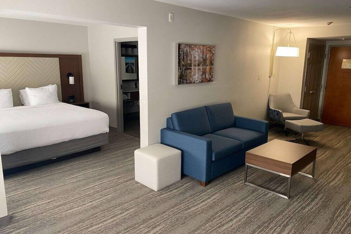 A hotel room with a bed, a blue sofa, a small table, and a chair.