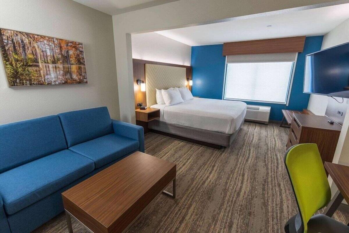 A hotel room with a bed, a blue sofa, a wooden coffee table, a desk with a chair, and a TV.
