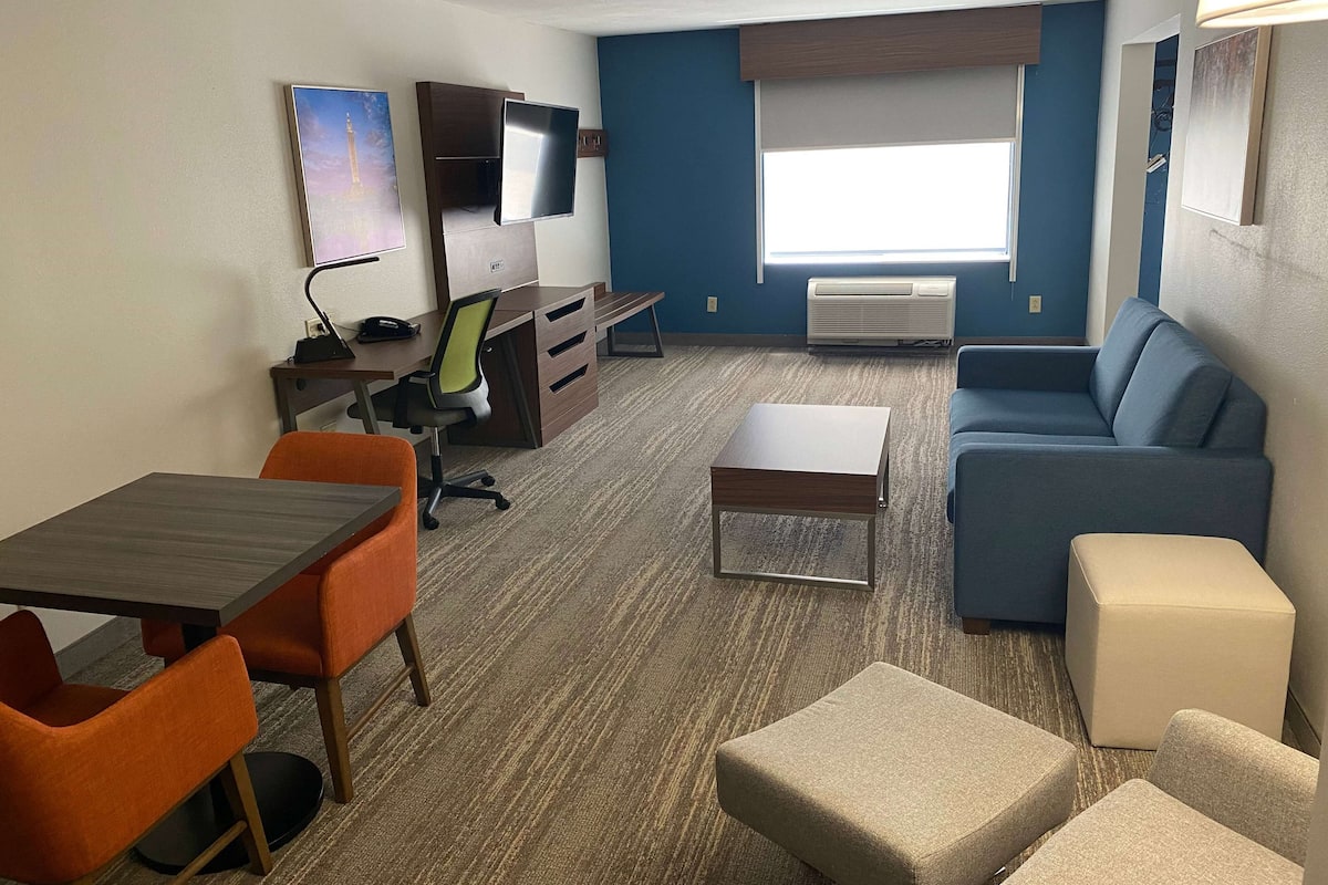 Habitación de hotel con escritorio, silla, sofá, otoman y televisor.