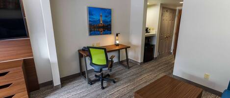 A hotel room with a desk, chair, and a painting of a cityscape.