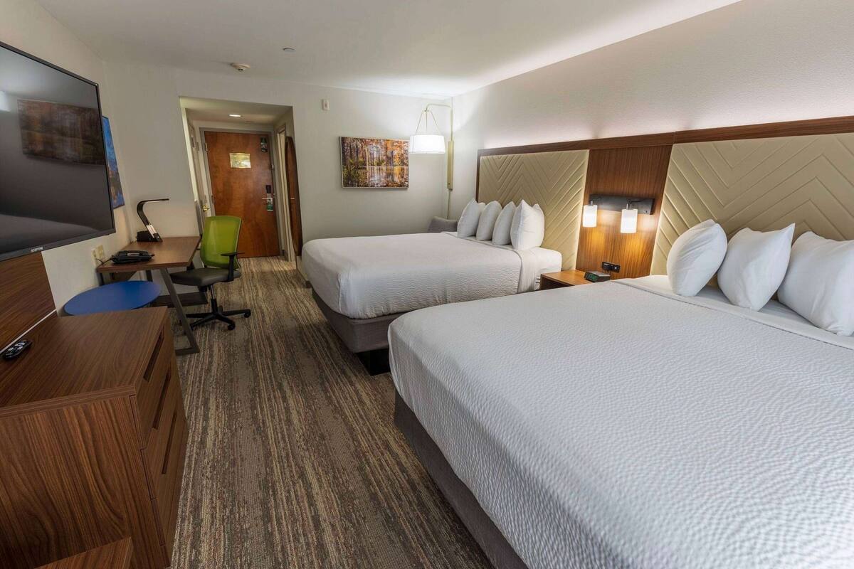 A hotel room with two beds, a desk with a chair, a television, and a painting on the wall.