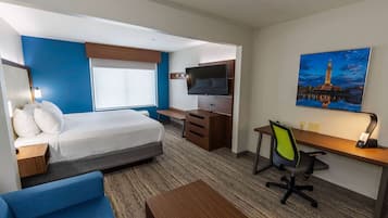 Quarto de hotel com cama, escrivaninha, cadeira, televisão e um quadro de uma torre.