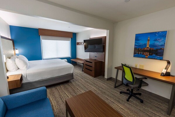Habitación de hotel con cama, escritorio, silla, televisión y un cuadro de una torre.