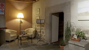 Una habitación acogedora con suelo de piedra, una lámpara, dos sillones, una mesita y una planta en maceta.