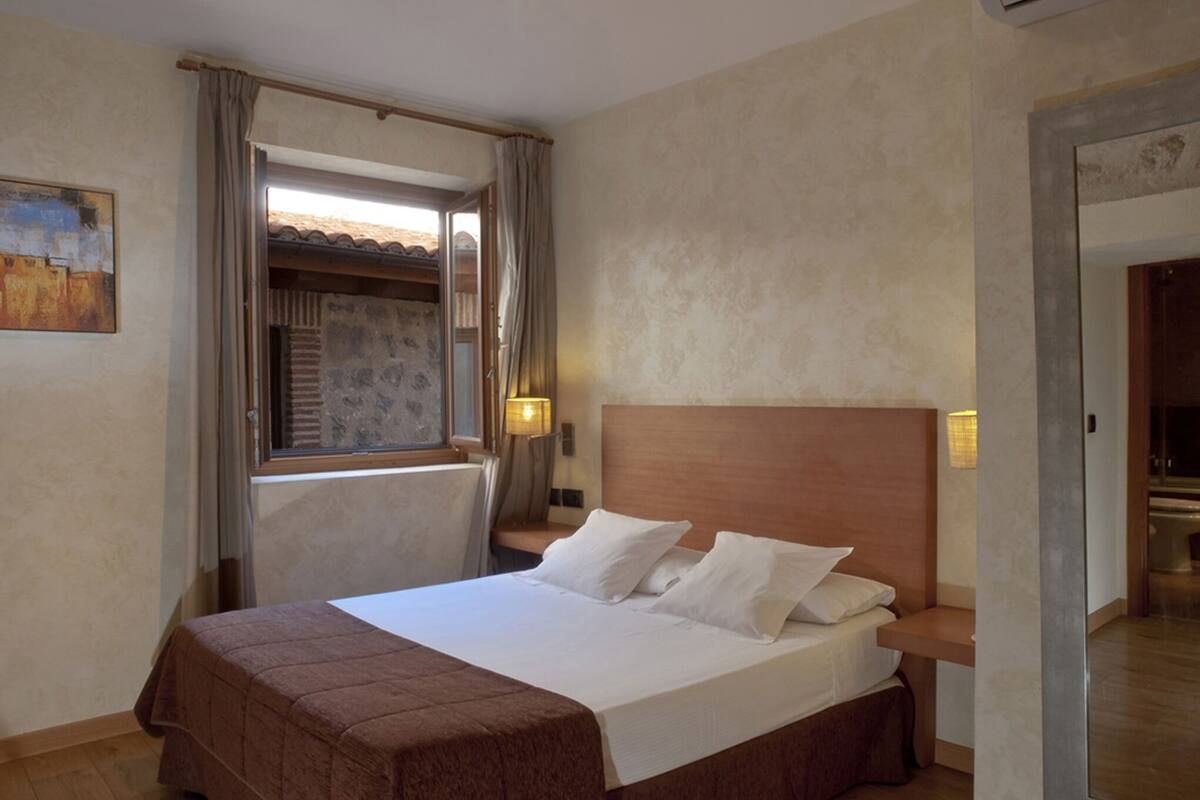 Une chambre à coucher avec un lit, une fenêtre avec des rideaux, une table de chevet avec une lampe et un tableau accroché au mur.