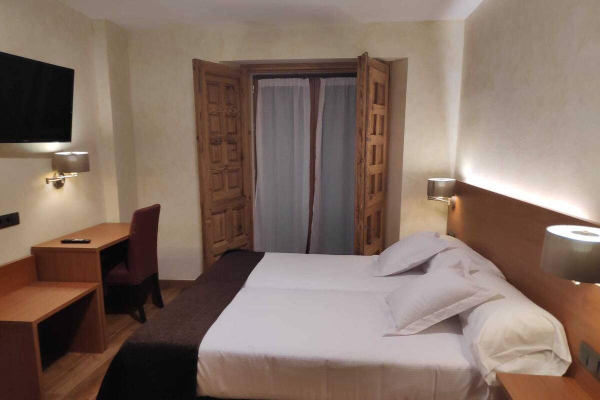 Une chambre d’hôtel avec un lit, un bureau, une chaise, une télévision et une porte avec des rideaux.