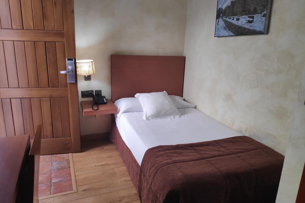 Une chambre d’hôtel avec une armoire en bois, une table de chevet avec une lampe, un téléphone et un lit avec du linge de lit blanc et une couverture marron.