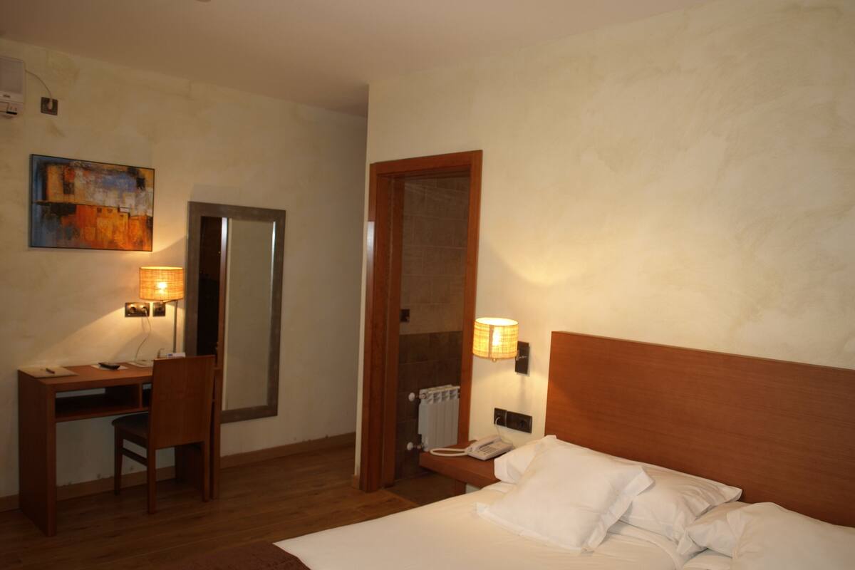 Une chambre d’hôtel avec un lit, un bureau, une chaise, une lampe et un tableau au mur.