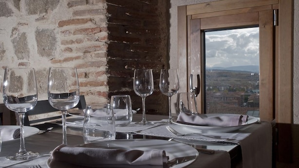Mesa de comedor dispuesta con copas de vino, platos y cubiertos, con vistas a un paisaje pintoresco a través de una ventana.