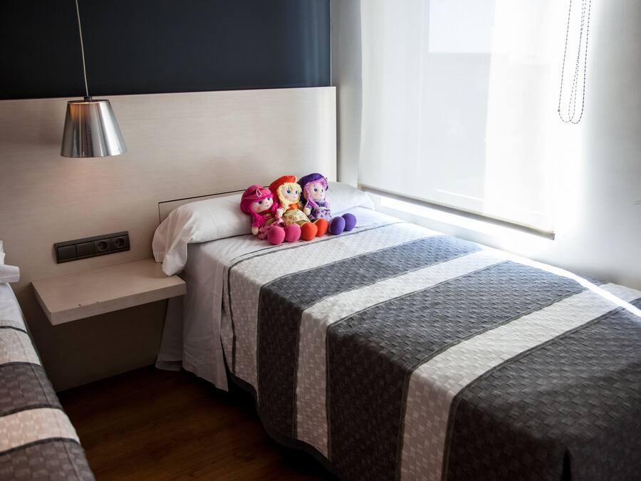 A hotel room with two beds, a bedside table, a lamp, and a window with curtains.