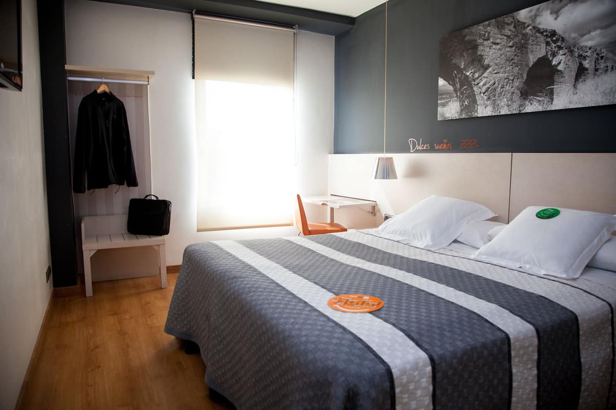Een hotelkamer met een bed, een bankje, een kapstok en een aan de muur hangend schilderij.