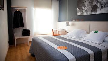 Een hotelkamer met een bed, een bankje, een kapstok en een aan de muur hangend schilderij.