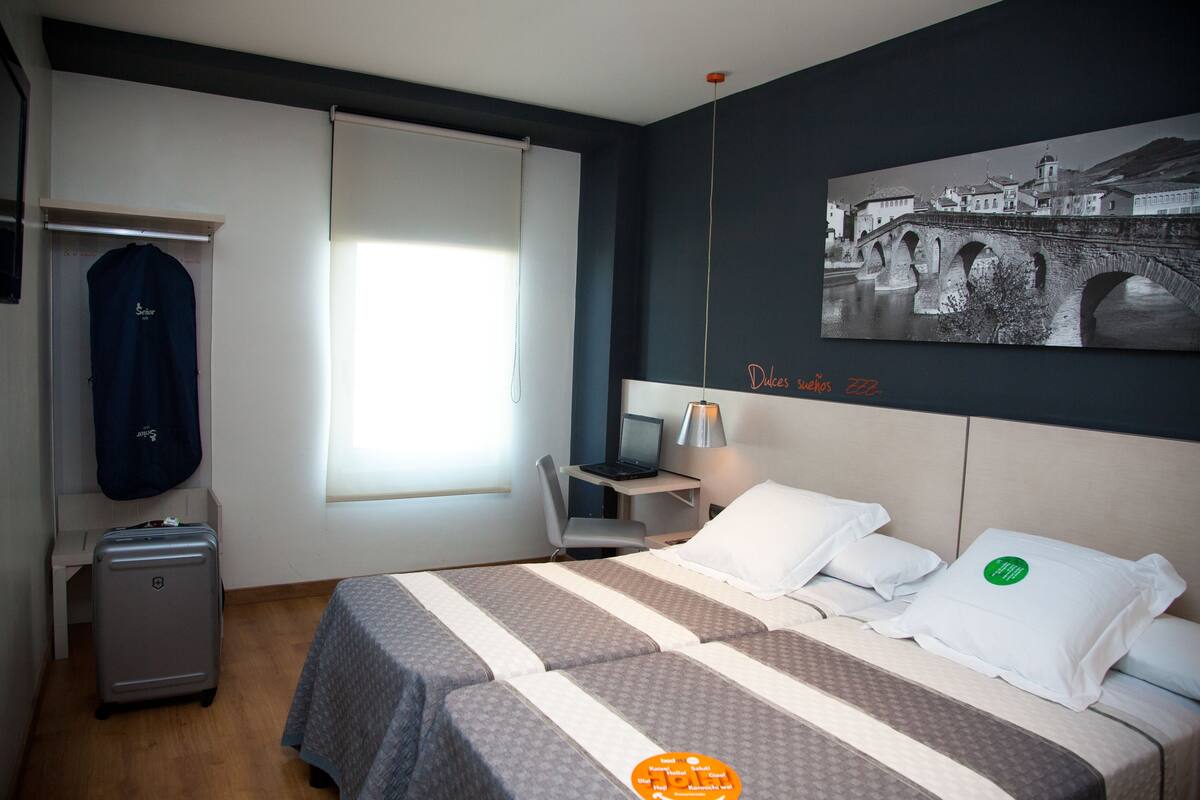 Een hotelkamer met een bed, een bureau, een stoel, een koffer en een schilderij aan de muur.