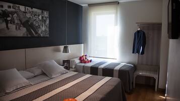 A hotel room with two beds, a large window, a hanging coat rack, and a wall-mounted television.