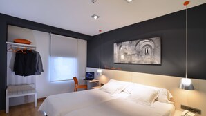 Une chambre d’hôtel moderne avec un grand lit, un bureau avec un ordinateur, une chaise et un tableau au mur.