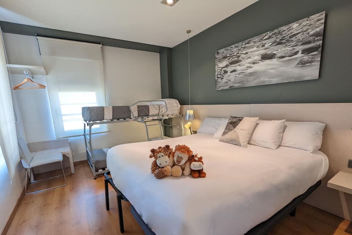 Een hotelkamer met een bed, bureau, stoel, garderobe en een schilderij aan de muur.