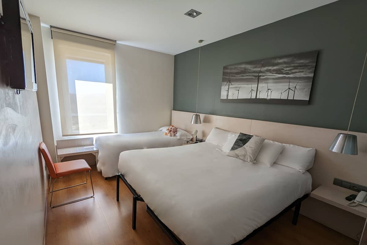 Een hotelkamer met twee bedden, een bureau, een stoel, een schilderij en een raam.
