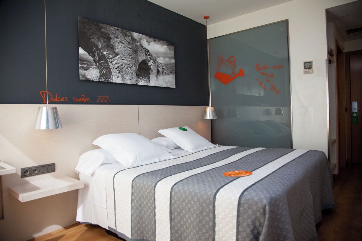 Un lit bien fait, recouvert d’une couvre-lit à rayures, une table de chevet avec une lampe et un tableau accroché au mur.