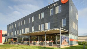 Un hôtel moderne doté d’un toit plat, de grandes fenêtres et d’un espace extérieur aménagé avec des tables et des chaises.
