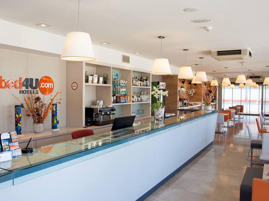 Zona de recepción de hotel con un mostrador de cristal, una máquina de café y diversas comodidades, como una planta, un jarrón y una exhibición de postales.