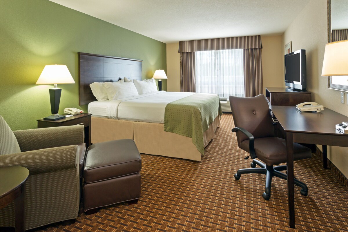 A hotel room with a bed, a desk, a chair, a telephone, and a television.