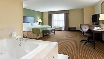 Habitación de hotel con una bañera grande, una cama con cabecera verde, un escritorio con computadora y televisor.