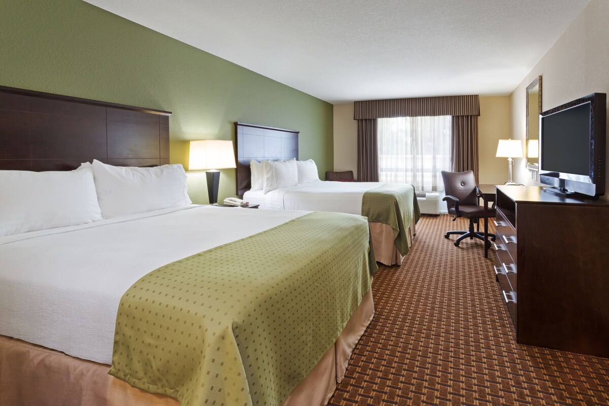 A hotel room with two beds, a desk, a TV, and a chair.