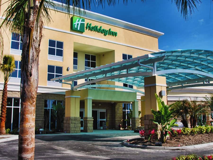 A Holiday Inn Express with a covered entrance, palm trees, and a clear blue sky.