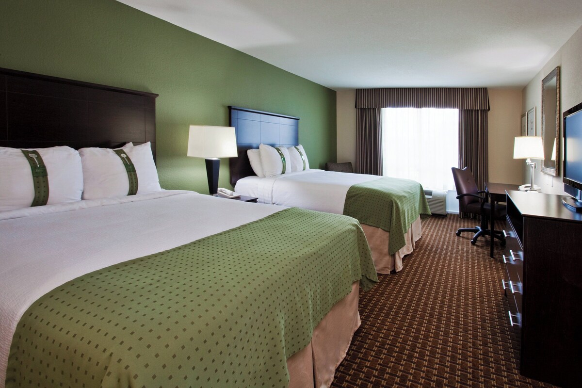 A hotel room with two beds, a desk, a chair, and a television.