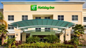 Un hôtel Holiday Inn avec un logo vert et blanc, une entrée couverte et des palmiers.