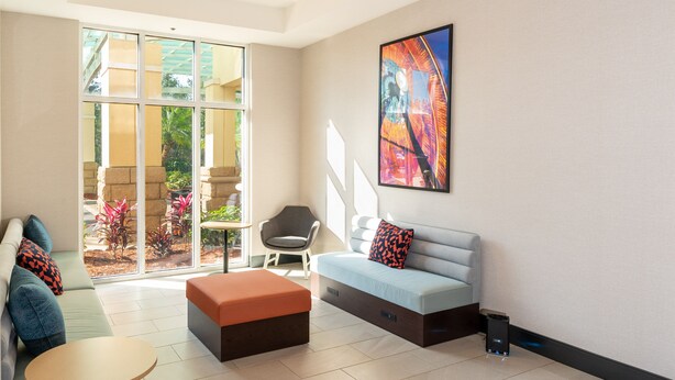 Een moderne woonkamer met een bank, poef en een klein tafeltje. Er is een fauteuil en een groot raam met uitzicht op groen.