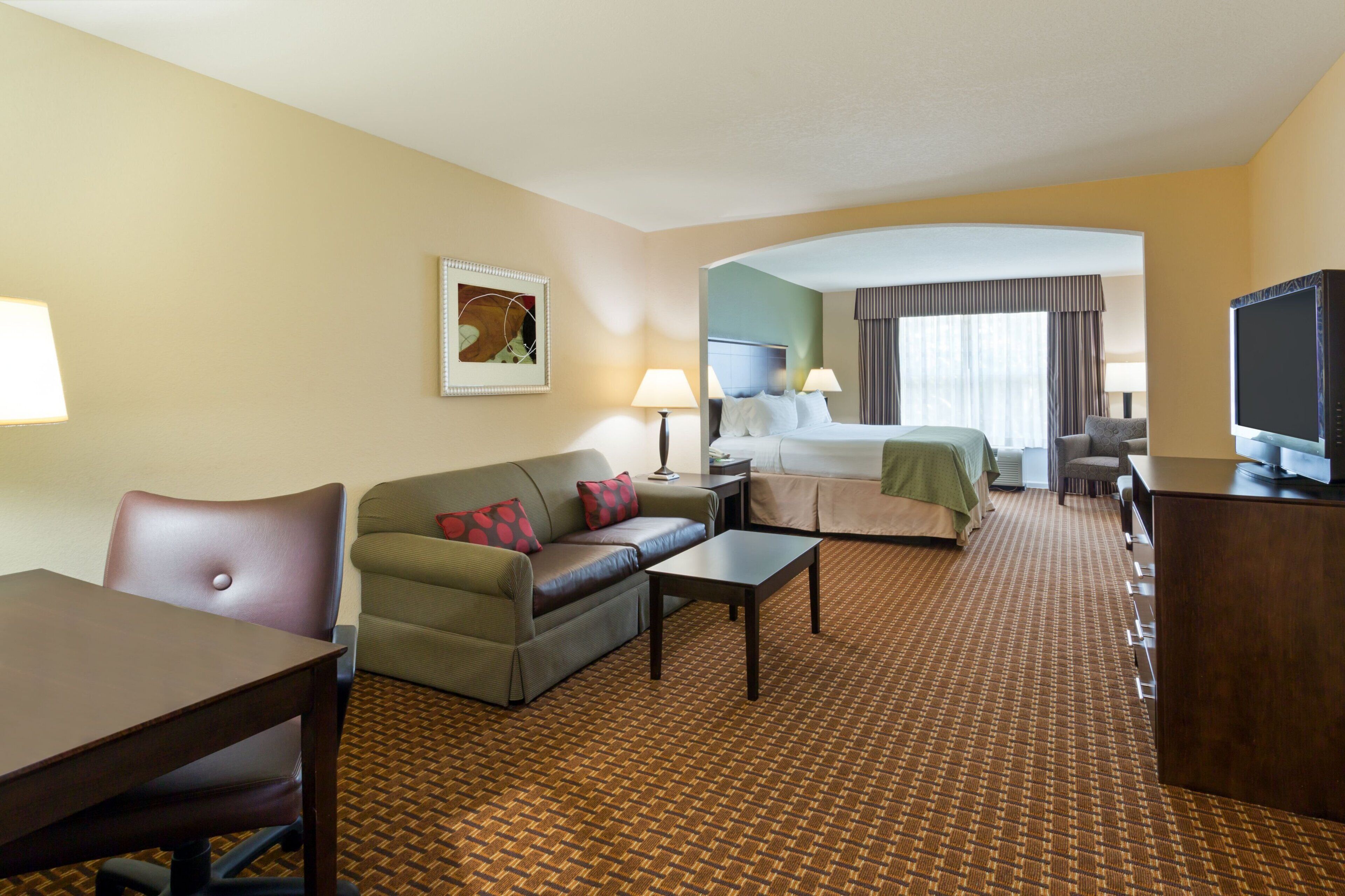 A hotel room with a bed, a sofa, a desk, a television, and a lamp.
