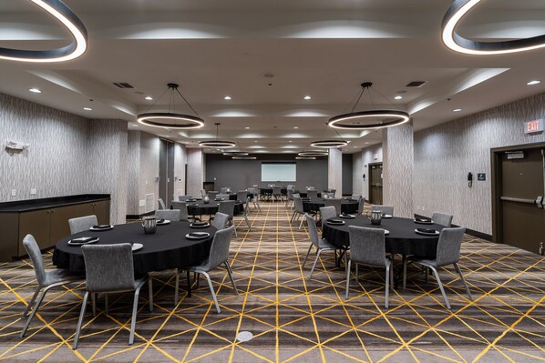 A conference room with a patterned carpet, round tables, and modern lighting fixtures. - Holiday Inn Daytona Beach LPGA Boulevard by IHG (Daytona Beach)