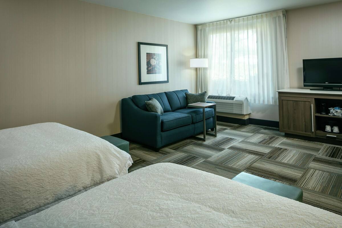 A hotel room with a bed, a sofa, a TV, and a window with curtains.