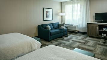 Quarto de hotel com cama, sofá, televisão e janela com cortinas.
