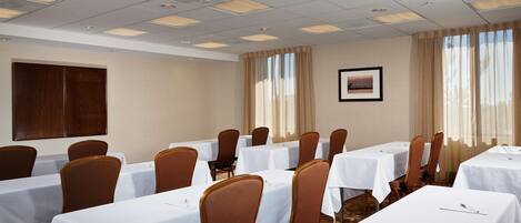A conference room with multiple tables and chairs, a large wooden panel on the wall, and a framed picture.