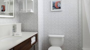 Une salle de bain moderne avec un lavabo blanc, un miroir et des toilettes. Un tableau encadré est accroché au mur, et il y a un porte-serviettes.