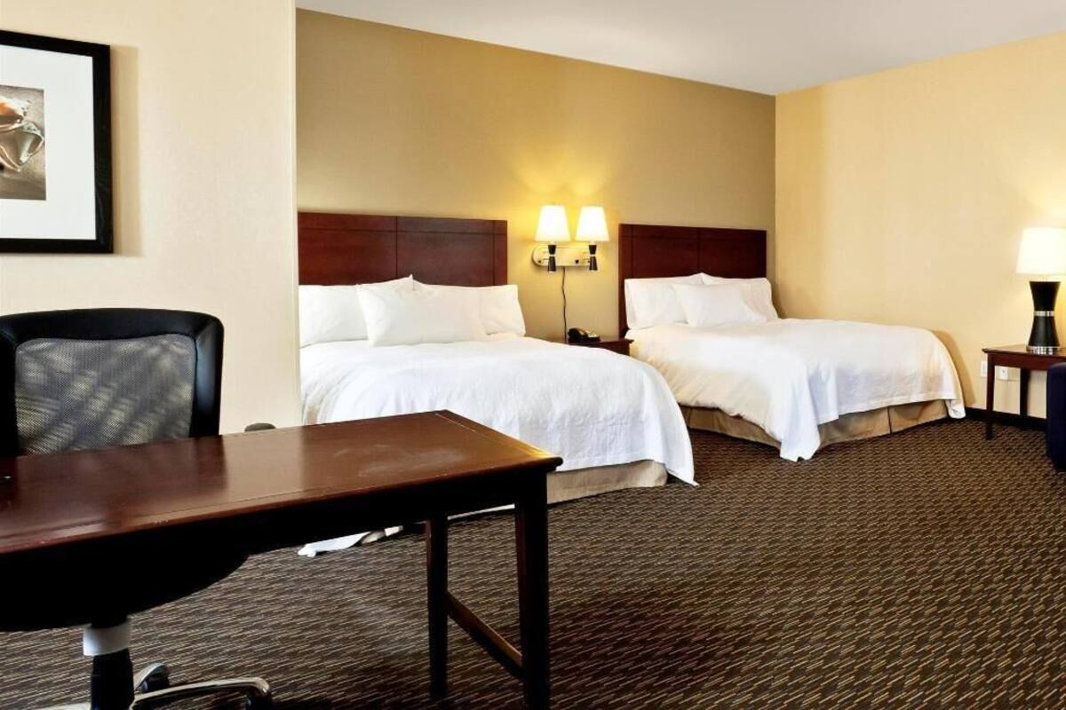 A hotel room with two beds, a desk, and a chair.