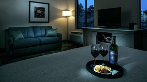 Habitación de hotel con sofá, televisión, botella de vino y copas sobre una bandeja.