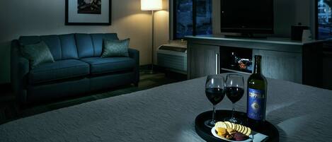 A hotel room with a sofa, a TV, a wine bottle, and glasses on a tray.