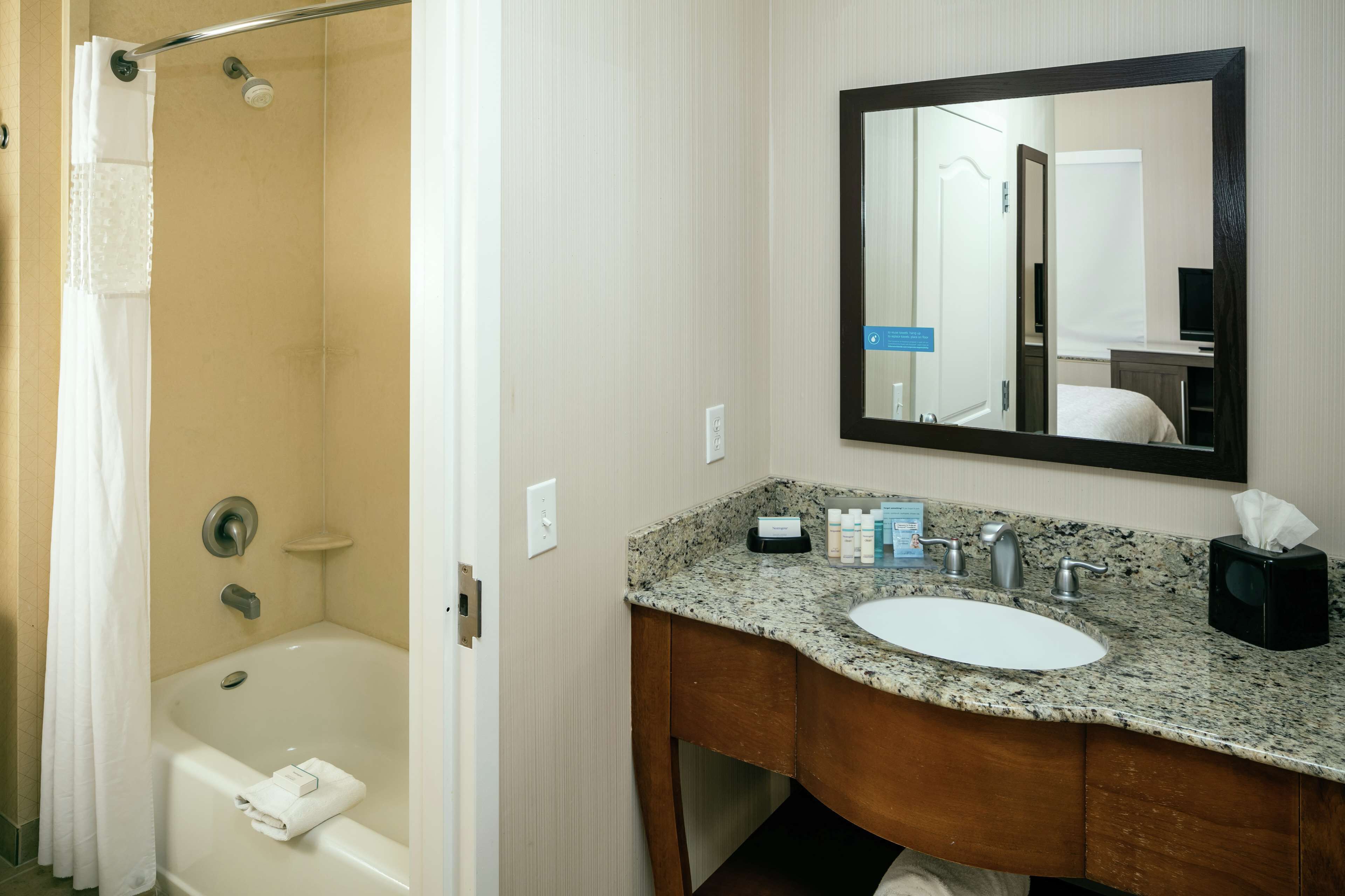 A bathroom with a bathtub, a sink, a mirror, and toiletries on the counter.