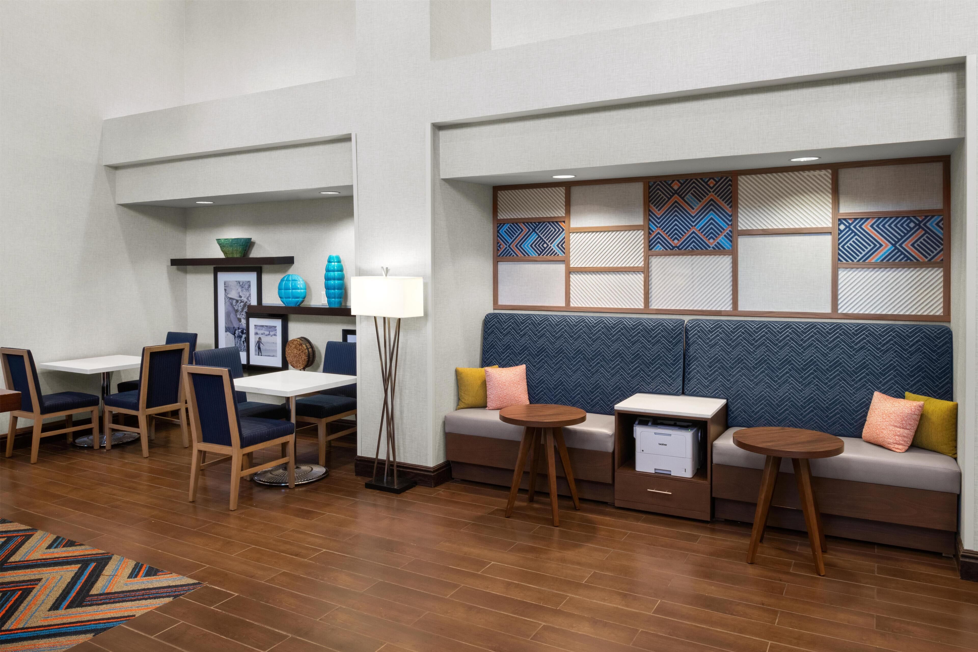 Et hotel lobby med siddeområde, borde og en dekorativ væg.
