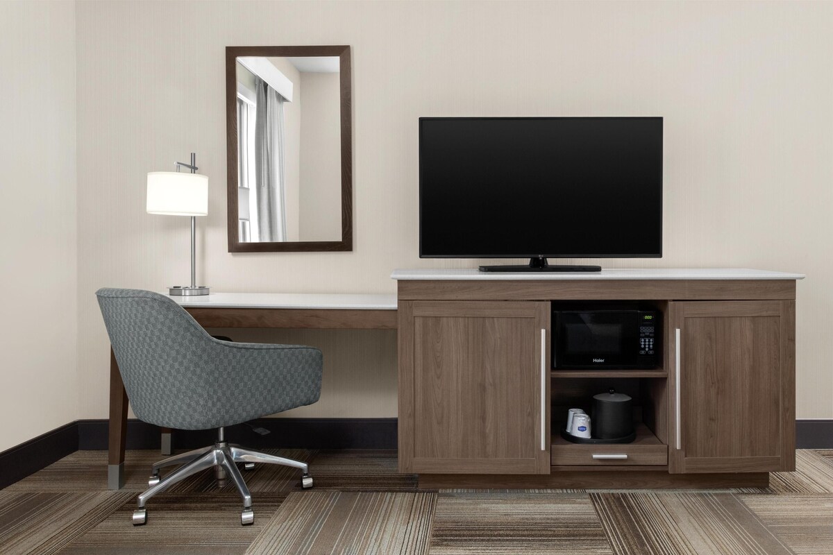 Hotelkamer met een houten bureau, een flatscreen televisie, een grijze bureaustoel, een magnetron en een lamp.