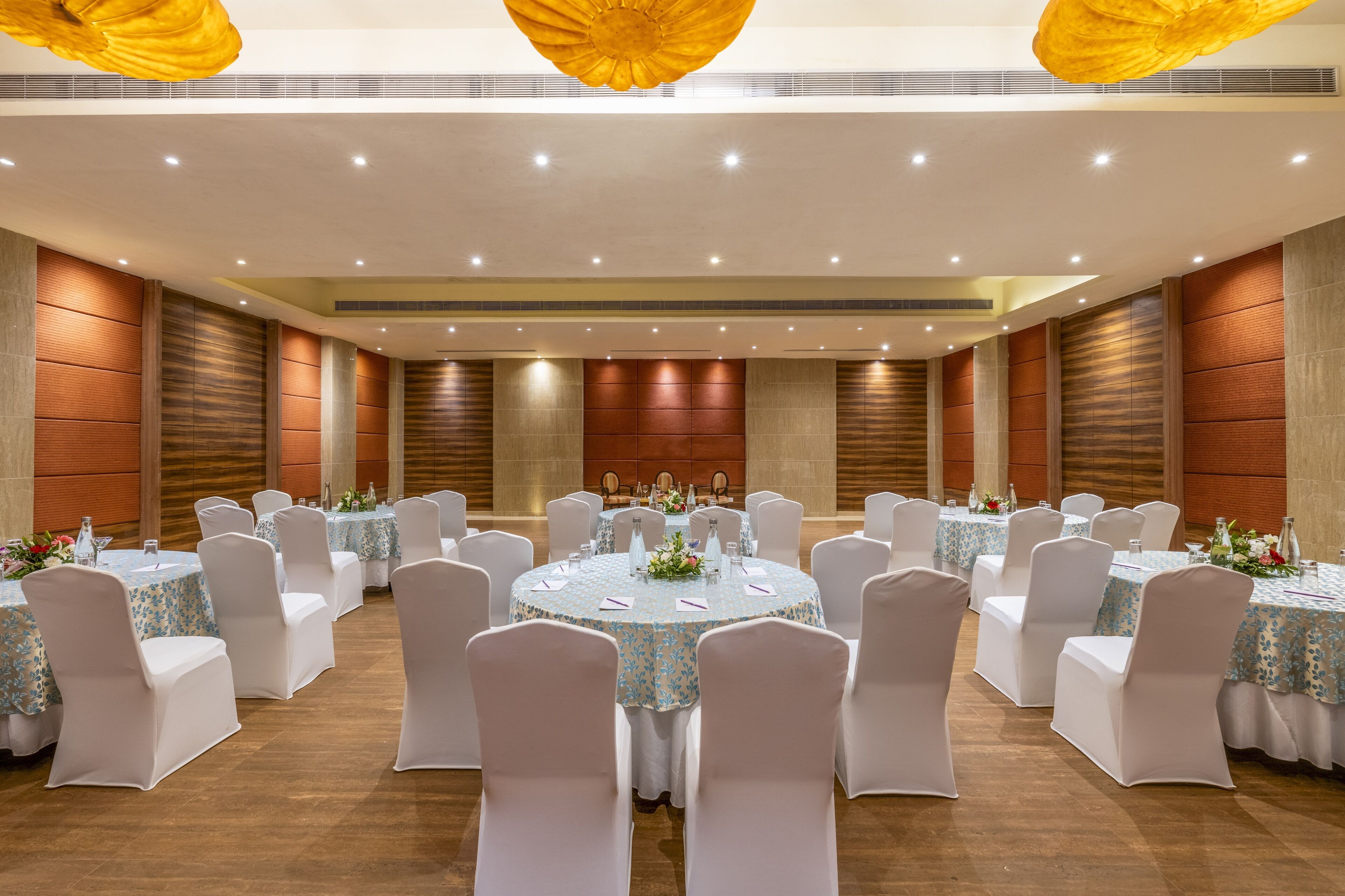 A banquet hall with round tables, white chairs, and floral centerpieces.