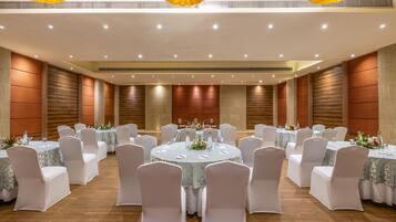 Uma sala de banquetes com mesas redondas, cadeiras brancas e centros de mesa florais.