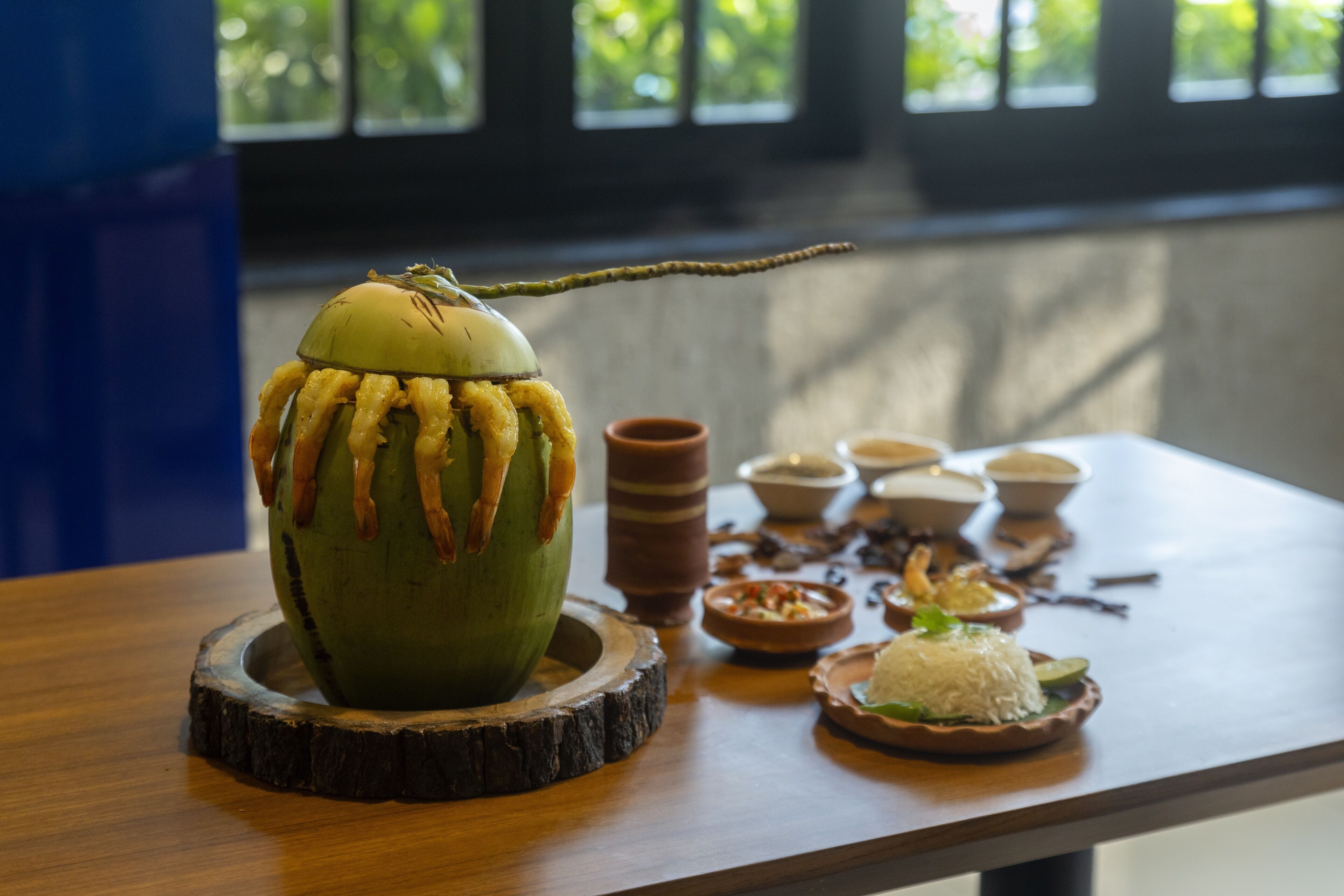 Une table ornée d’un centre de table sculpté en noix de coco, entourée de petits bols remplis de nourriture et d’un plateau en bois.
