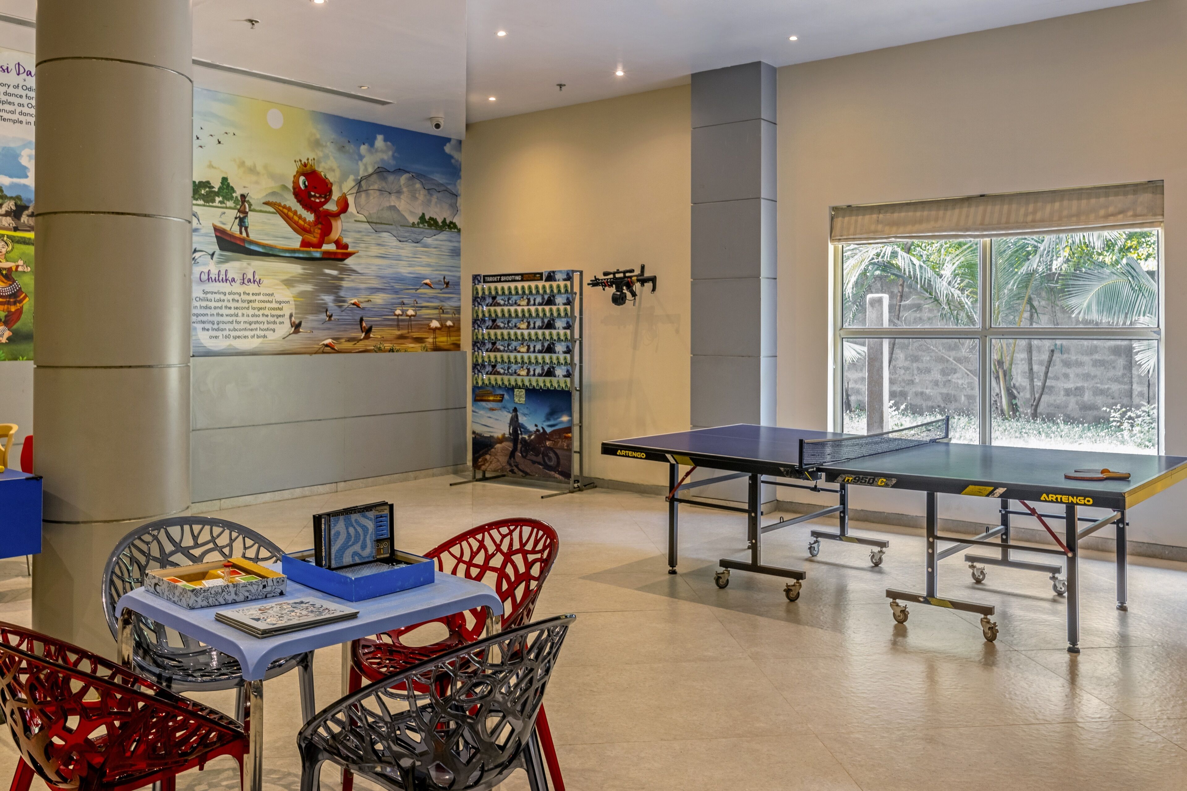 A room with a ping pong table, chairs, a bookshelf, and a mural.