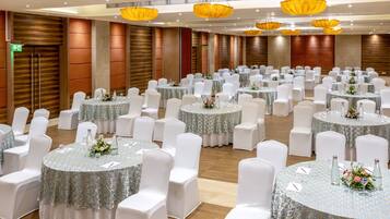 Uma sala de banquetes com mesas redondas, cadeiras brancas e arranjos florais.