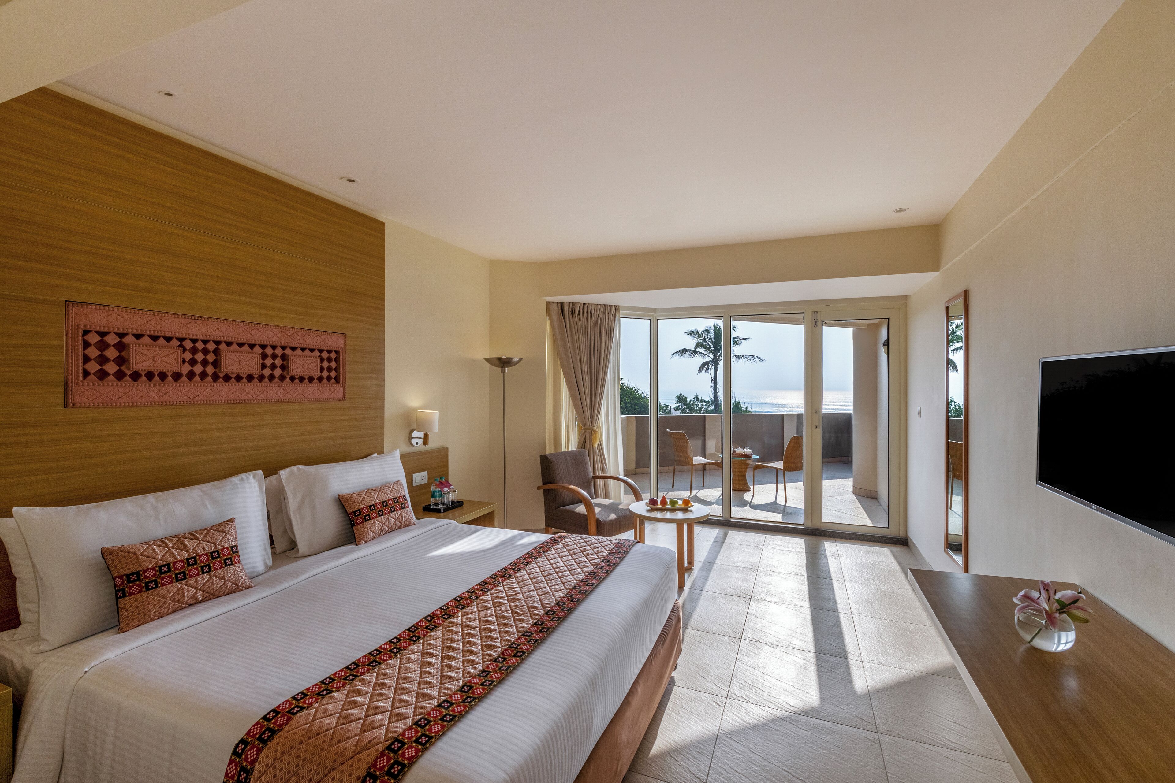 Ein Hotelzimmer mit einem großen Bett, einem Fernseher, einem Balkon mit Blick und einer Essecke.