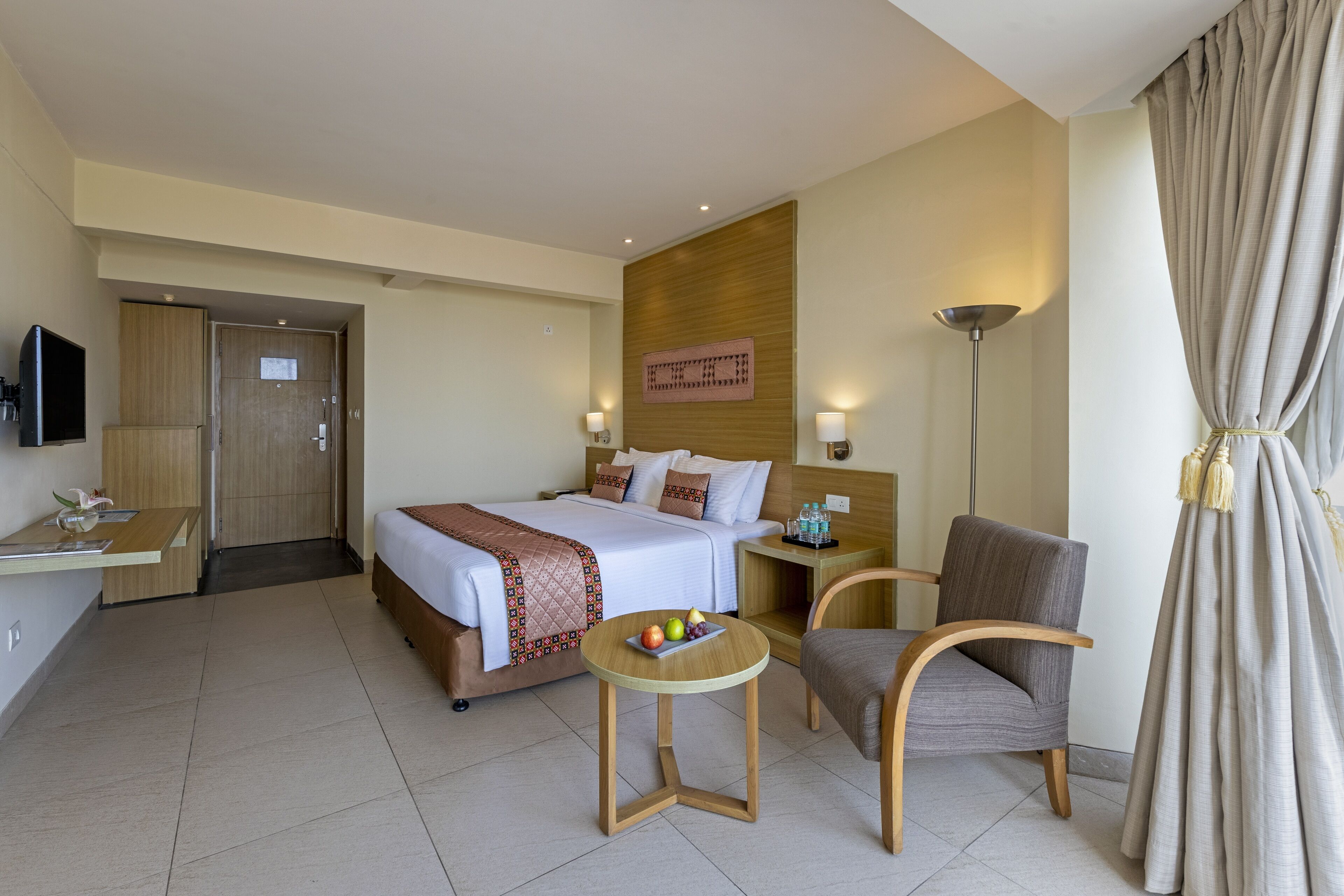 A hotel room with a bed, bedside table, chair, and a small table with fruit.